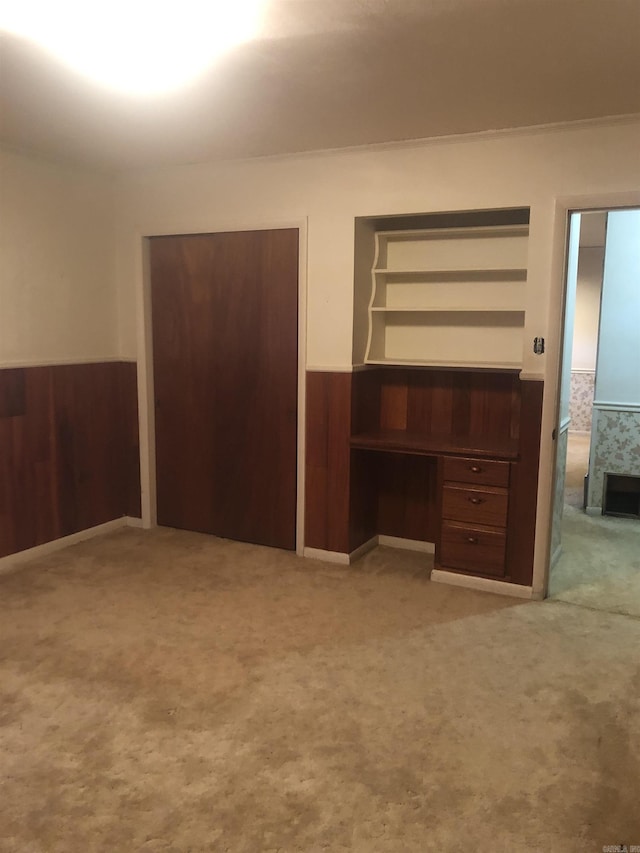 unfurnished bedroom with light colored carpet, wainscoting, wooden walls, and built in study area