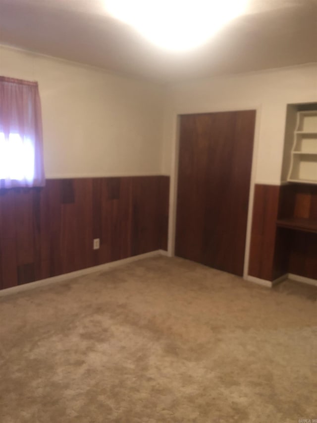 unfurnished bedroom with a wainscoted wall, wood walls, and carpet flooring