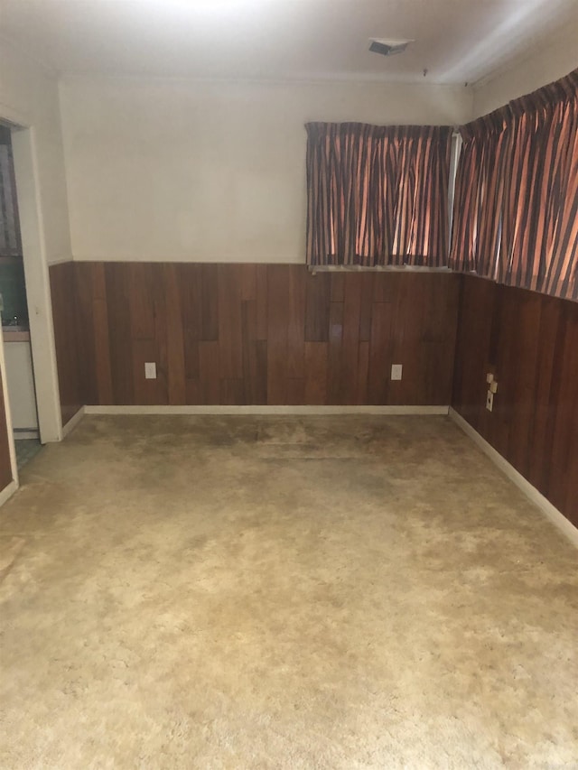 empty room featuring a wainscoted wall, visible vents, and wooden walls