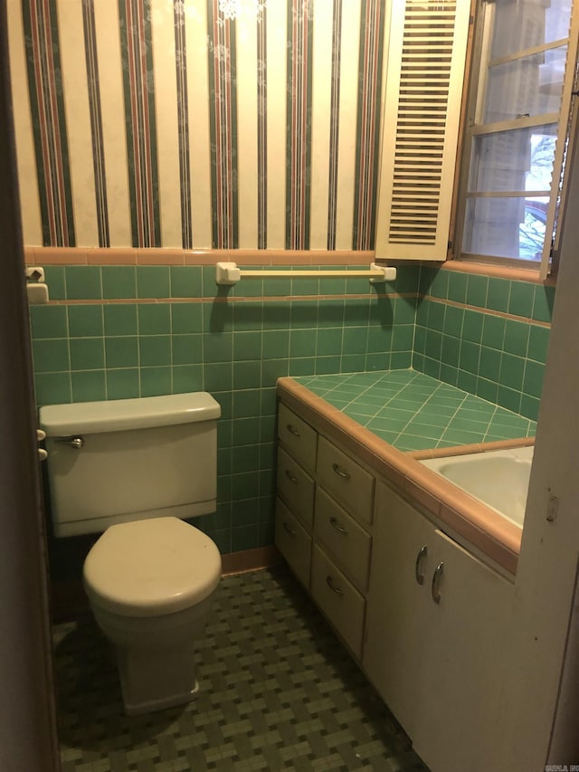 half bathroom with toilet, vanity, tile walls, wainscoting, and wallpapered walls