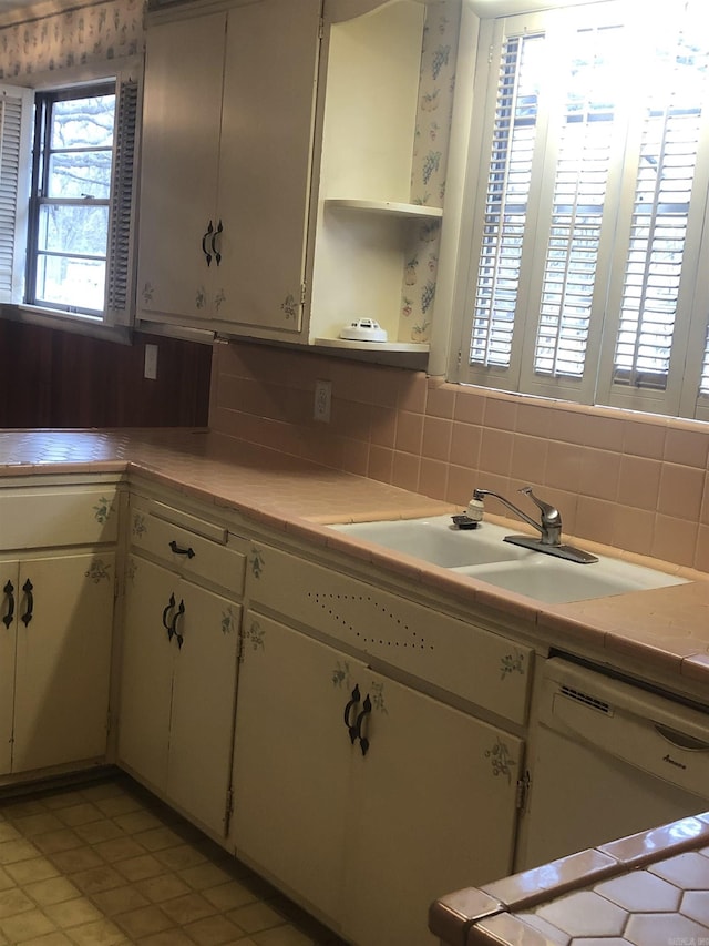 kitchen with white dishwasher, a sink, backsplash, and open shelves