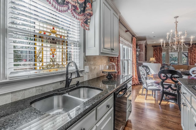 kitchen featuring dark wood-style floors, a notable chandelier, backsplash, a sink, and dark stone countertops