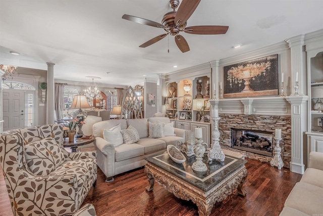 living area featuring a stone fireplace, ceiling fan with notable chandelier, wood finished floors, ornamental molding, and ornate columns