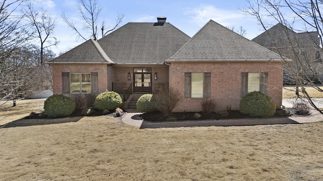 view of front facade featuring french doors, brick siding, a chimney, a shingled roof, and a front lawn