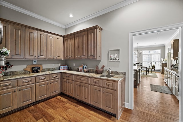 kitchen with light stone counters, ornamental molding, a sink, wood finished floors, and a chandelier