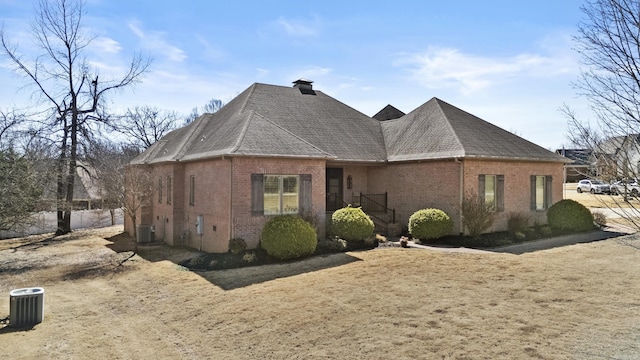 view of front of house featuring roof with shingles, central AC, and brick siding