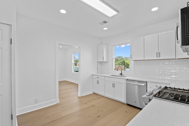 kitchen featuring visible vents, decorative backsplash, appliances with stainless steel finishes, white cabinetry, and a sink