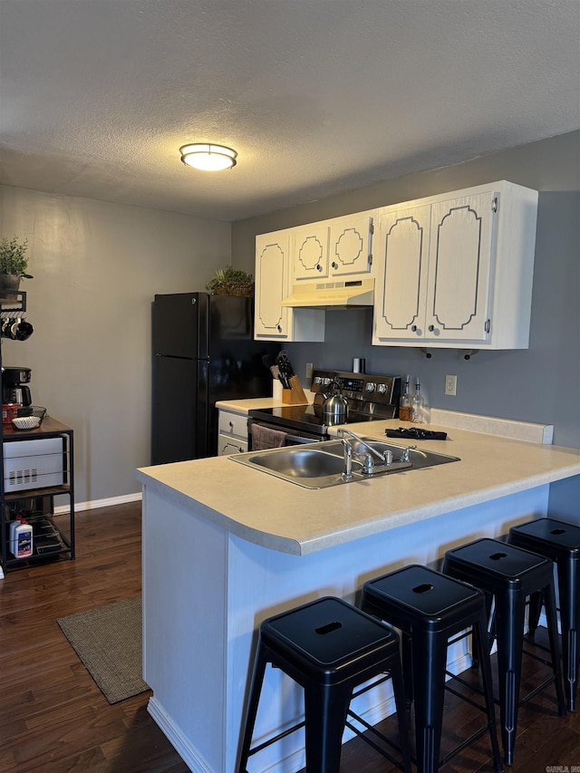 kitchen featuring under cabinet range hood, a peninsula, dark wood-style flooring, freestanding refrigerator, and stainless steel range with electric stovetop