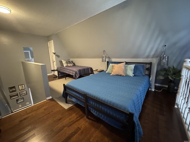 bedroom with vaulted ceiling, wood finished floors, and baseboards