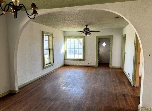 unfurnished living room featuring a textured ceiling, baseboards, wood finished floors, and ceiling fan with notable chandelier