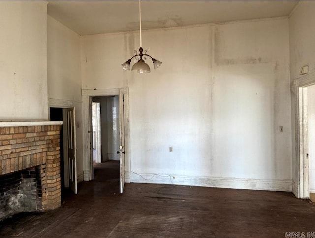 unfurnished dining area featuring a towering ceiling, a brick fireplace, and wood finished floors