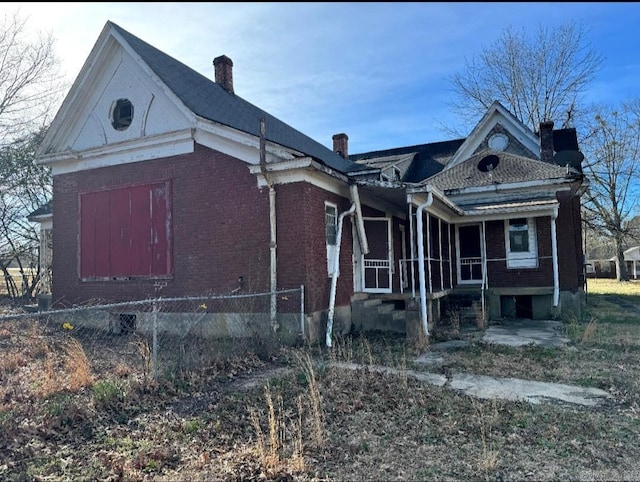 view of front of house with covered porch, a chimney, fence, and brick siding