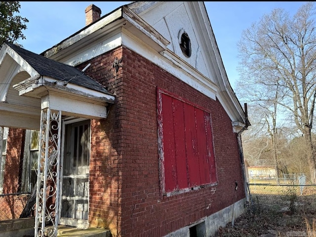 view of property exterior with a chimney, fence, and brick siding