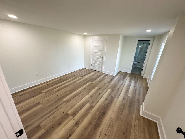 unfurnished bedroom featuring recessed lighting, ensuite bathroom, baseboards, and wood finished floors