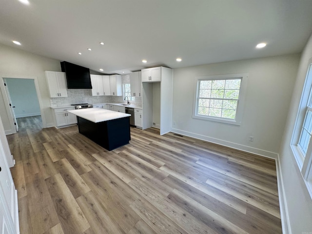 kitchen featuring a kitchen island, a sink, light countertops, ventilation hood, and tasteful backsplash