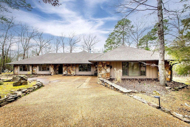 view of front of home featuring a shingled roof, stone siding, and driveway