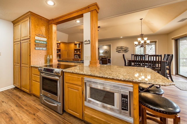 kitchen featuring light stone counters, a kitchen breakfast bar, appliances with stainless steel finishes, dark wood finished floors, and ornate columns