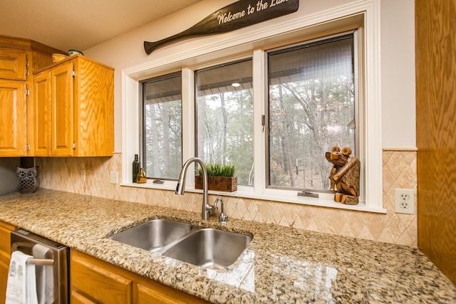 kitchen with light stone countertops, dishwasher, brown cabinetry, and a sink