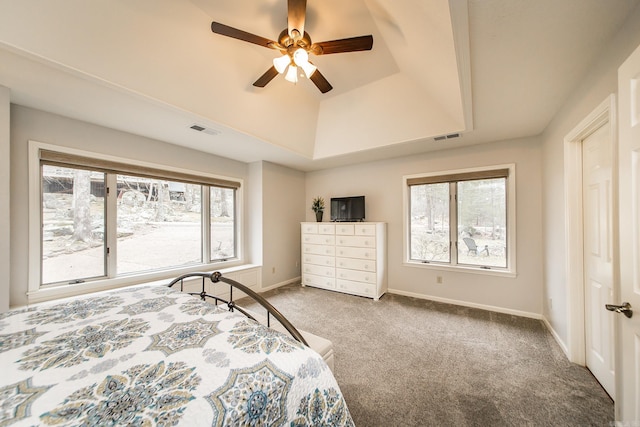 carpeted bedroom featuring a ceiling fan, a tray ceiling, visible vents, and baseboards