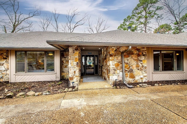 entrance to property with stone siding and a shingled roof