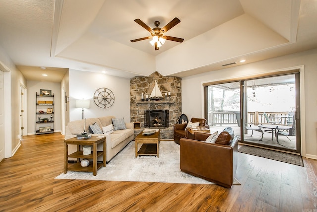 living area featuring baseboards, visible vents, a raised ceiling, wood finished floors, and a stone fireplace