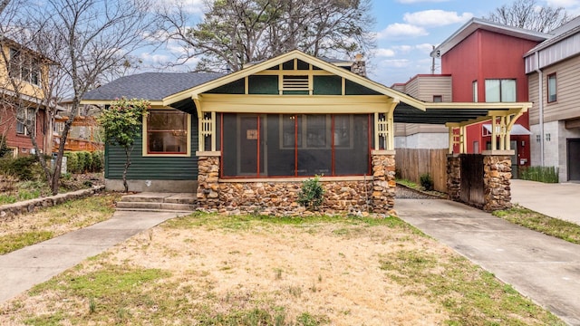 view of front of home with stone siding, a front yard, and a sunroom