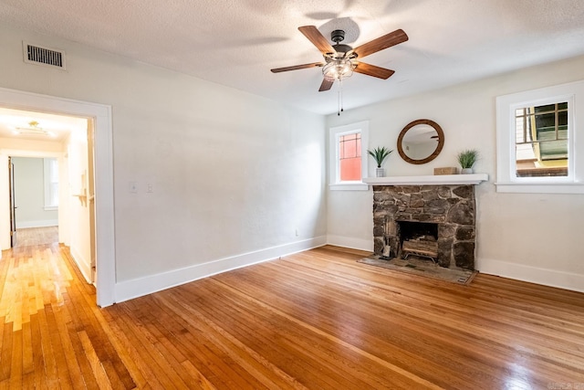 unfurnished living room with baseboards, visible vents, hardwood / wood-style floors, a textured ceiling, and a fireplace