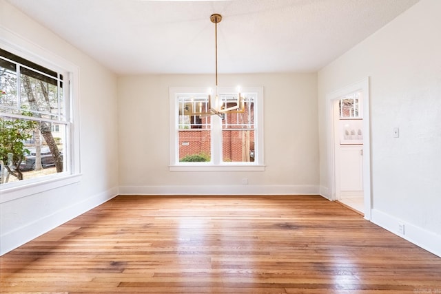 unfurnished dining area with a chandelier, light wood-type flooring, and baseboards