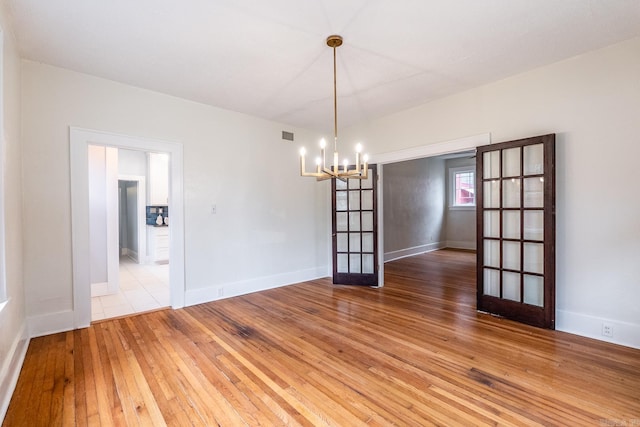 spare room featuring french doors, visible vents, a chandelier, baseboards, and hardwood / wood-style flooring