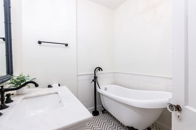 full bath with a soaking tub, wainscoting, a sink, and a decorative wall