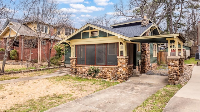 view of front of property with a sunroom, stone siding, central AC unit, and roof with shingles