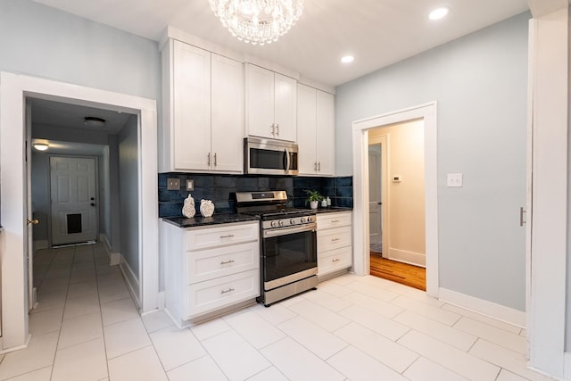 kitchen featuring a notable chandelier, stainless steel appliances, baseboards, white cabinets, and decorative backsplash