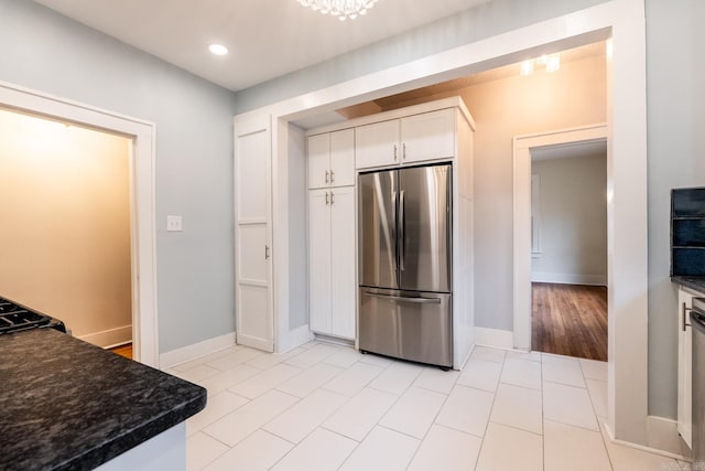 kitchen with light tile patterned floors, white cabinetry, baseboards, freestanding refrigerator, and dark countertops