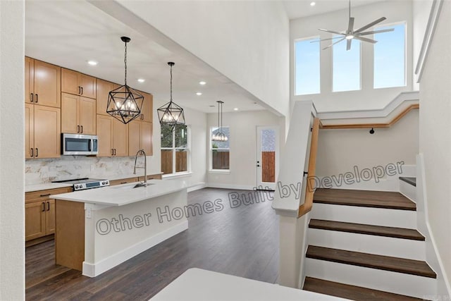 kitchen featuring electric stove, a center island with sink, tasteful backsplash, stainless steel microwave, and a sink