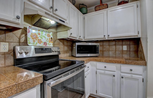 kitchen with appliances with stainless steel finishes, under cabinet range hood, white cabinetry, and tile countertops