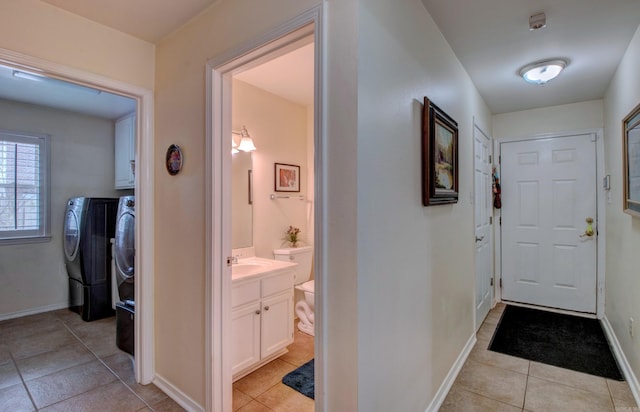 hallway with light tile patterned flooring, a sink, baseboards, and separate washer and dryer