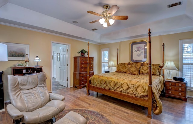 bedroom with visible vents, ornamental molding, wood finished floors, ensuite bathroom, and a tray ceiling