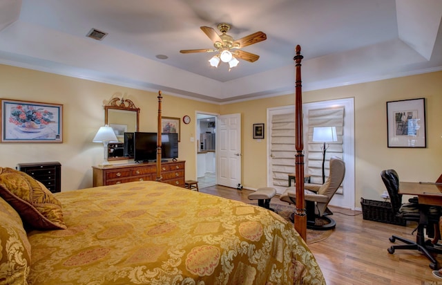 bedroom with ceiling fan, wood finished floors, visible vents, baseboards, and a tray ceiling