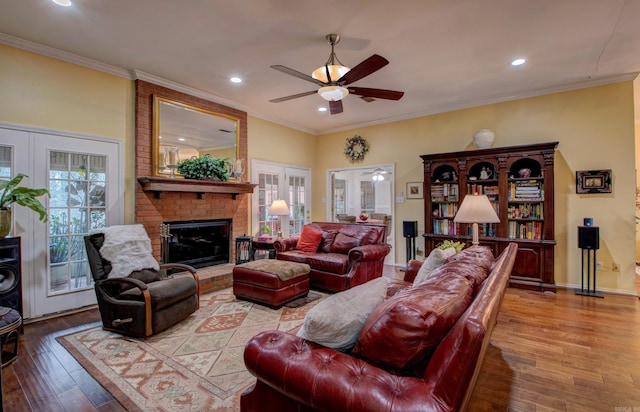 living area with a brick fireplace, french doors, crown molding, and hardwood / wood-style floors