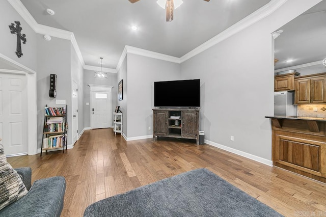 living area with ornamental molding, ceiling fan with notable chandelier, baseboards, and hardwood / wood-style flooring