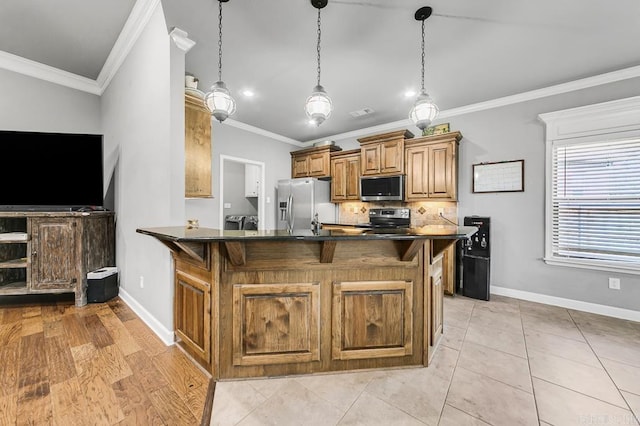 kitchen featuring dark countertops, ornamental molding, brown cabinets, stainless steel appliances, and a kitchen bar