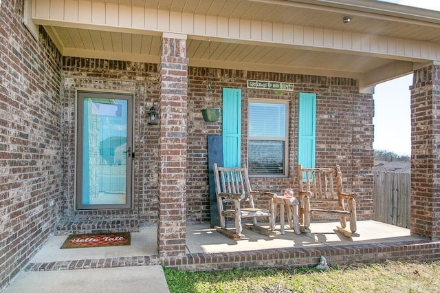 view of exterior entry featuring covered porch and brick siding