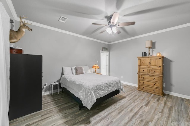 bedroom featuring ceiling fan, light wood-style flooring, visible vents, baseboards, and ornamental molding