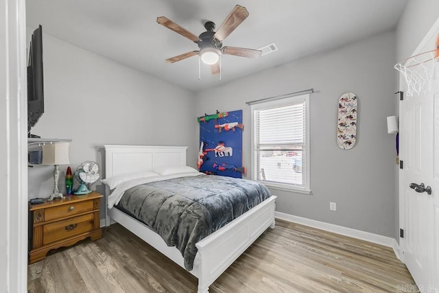 bedroom with a ceiling fan, visible vents, baseboards, and wood finished floors
