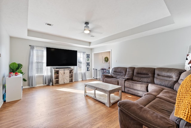 living room featuring a raised ceiling, visible vents, and light wood-style flooring