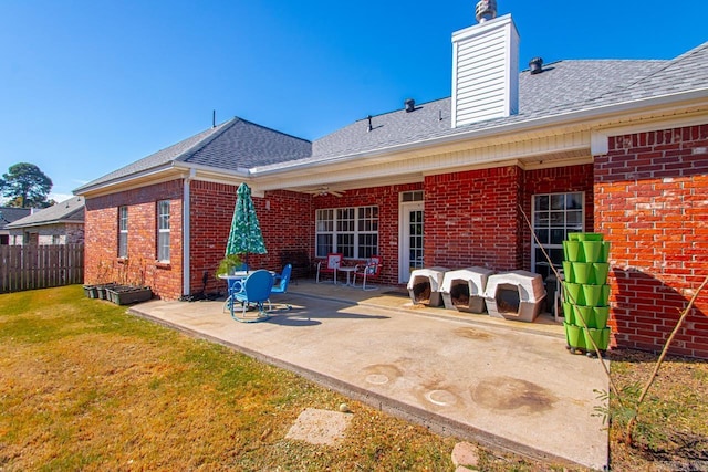 rear view of property featuring brick siding, fence, a yard, roof with shingles, and a patio area