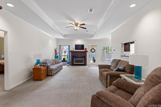 living area featuring visible vents, a raised ceiling, light colored carpet, crown molding, and a fireplace