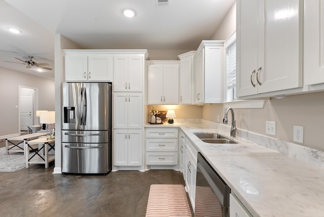 kitchen featuring a sink, a ceiling fan, white cabinets, appliances with stainless steel finishes, and light stone countertops