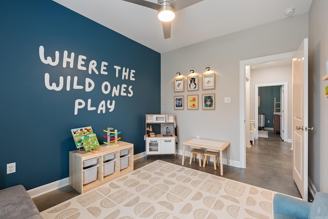 game room with a ceiling fan, an accent wall, finished concrete flooring, and baseboards