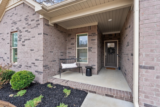 view of exterior entry featuring covered porch and brick siding